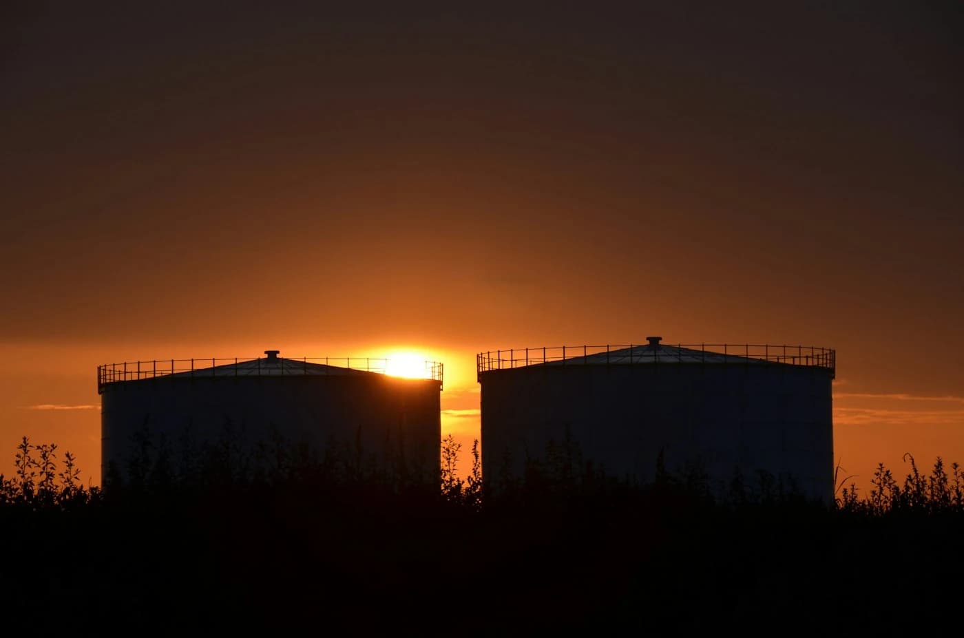 Bulk storage tanks silhouetted against a sunset